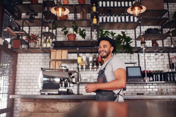 Indoor shot of happy young bar owner standing at the counter and looking away smiling